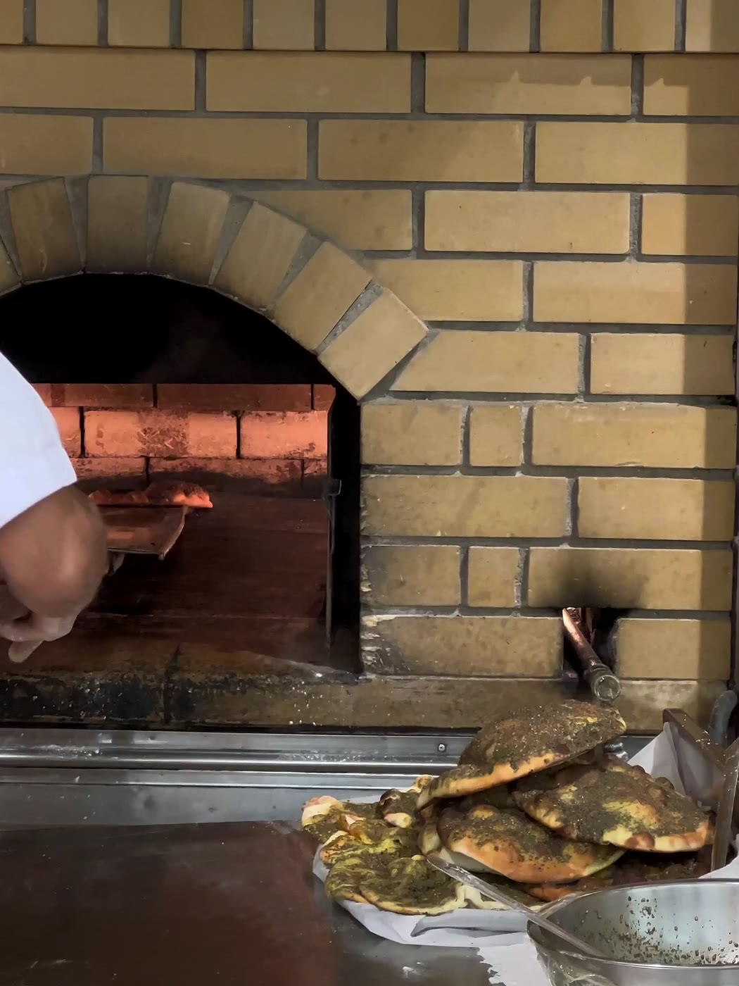 Un four voûté en briques, des galettes dorées empilées devant sa bouche.