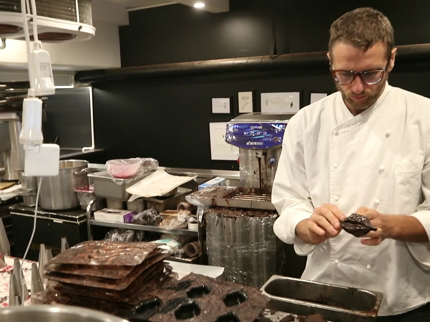 Un pâtissier en veste blanche façonne une pièce en chocolat dans son laboratoire.