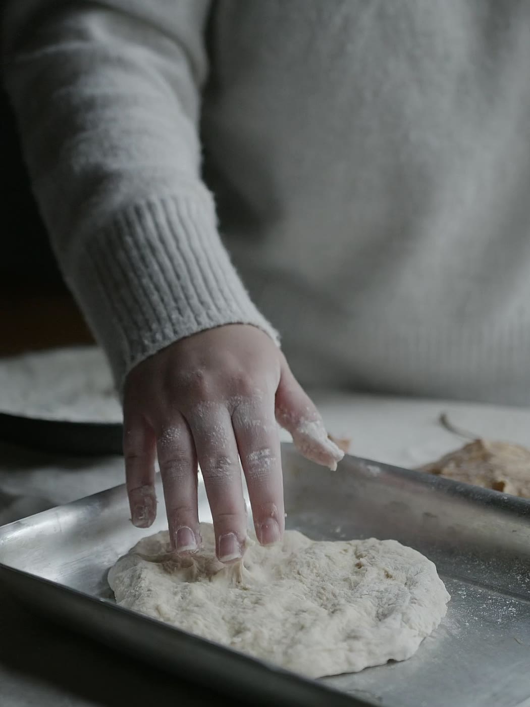 Une main farinée étale une pâte à pain sur une plaque de cuisson.