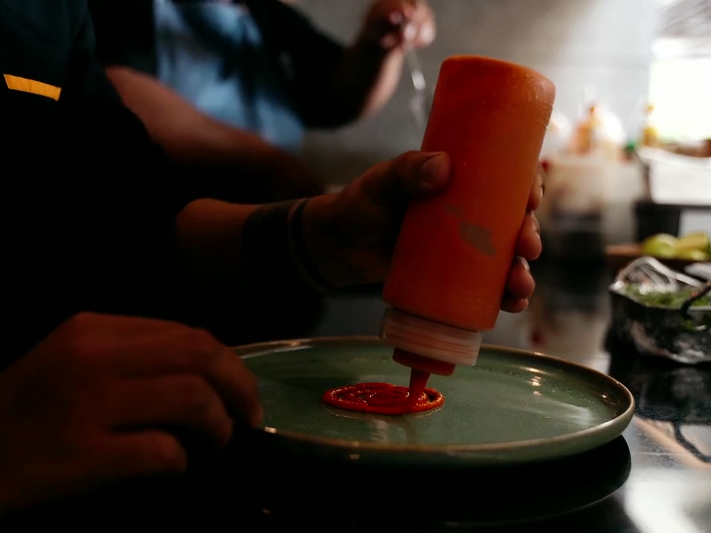 Un cuisinier trace un cercle de sauce orangée au centre d’une assiette en céramique verte.