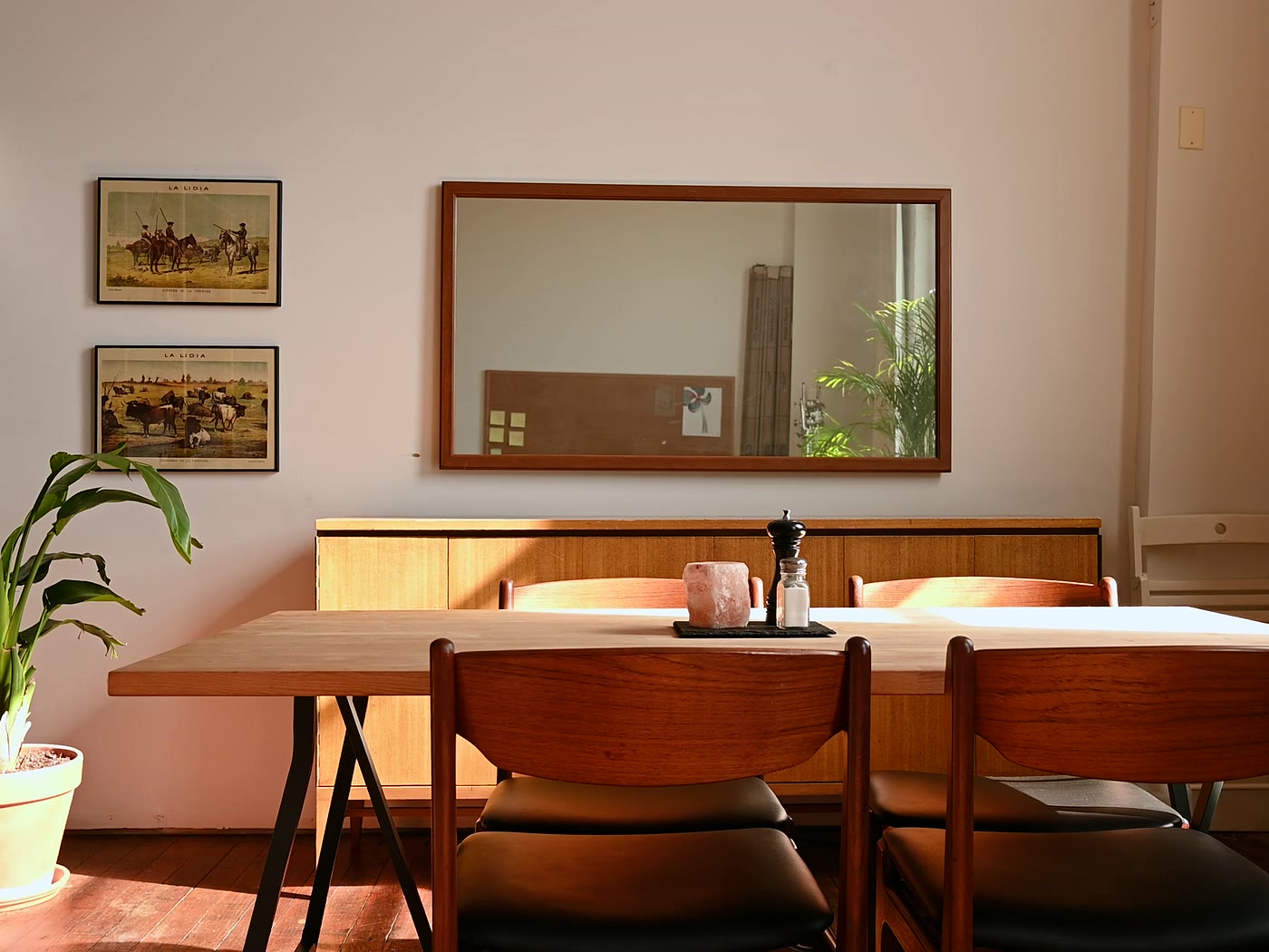 Salle à manger baignée de soleil : enfilade basse en bois blond, grande table et chaises au dossier de bois cintré, miroir encadré de bois au mur.