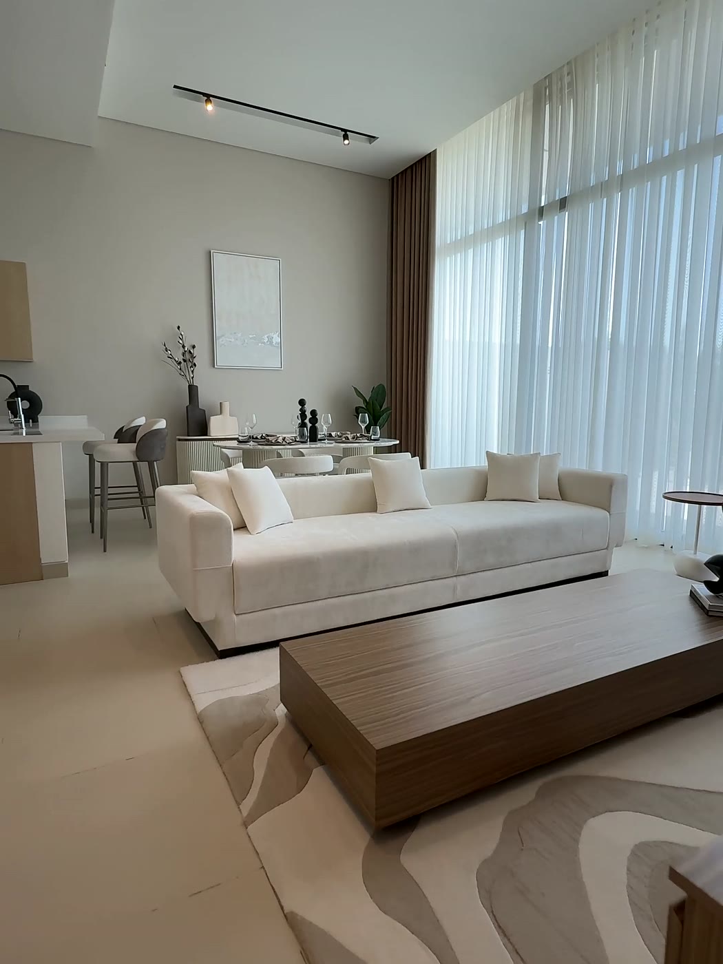 Séjour lumineux aux tons crème&nbsp;: canapé blanc, table basse en bois, grands voilages et une toile claire accrochée au mur.